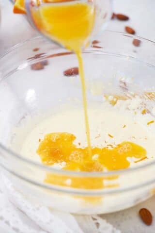 pouring fresh orange juice into cake batter in a bowl