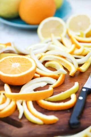orange and lemon peel on a cutting board next to an orange slice and a knife