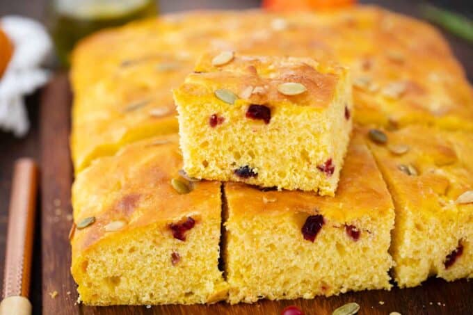a slice of pumpkin focaccia wit cranberries on top of the whole focaccia in a baking sheet