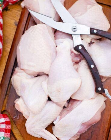 overhead shot of a whole chicken cut into pieces on a cutting board with kitchen scissors on top