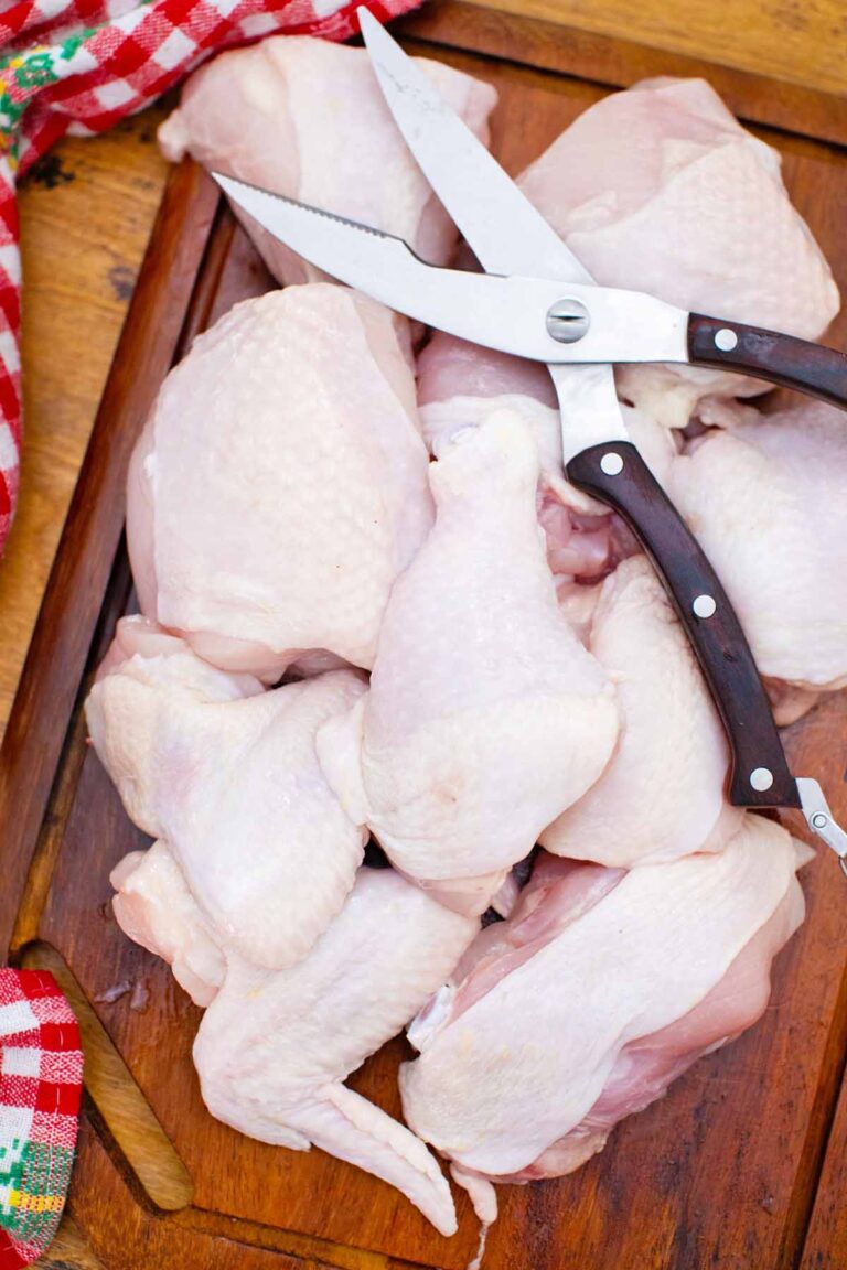 overhead shot of a whole chicken cut into pieces on a cutting board with kitchen scissors on top