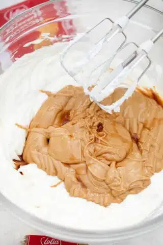 adding cookie butter to beaten cream cheese and a mixer on top of the bowl