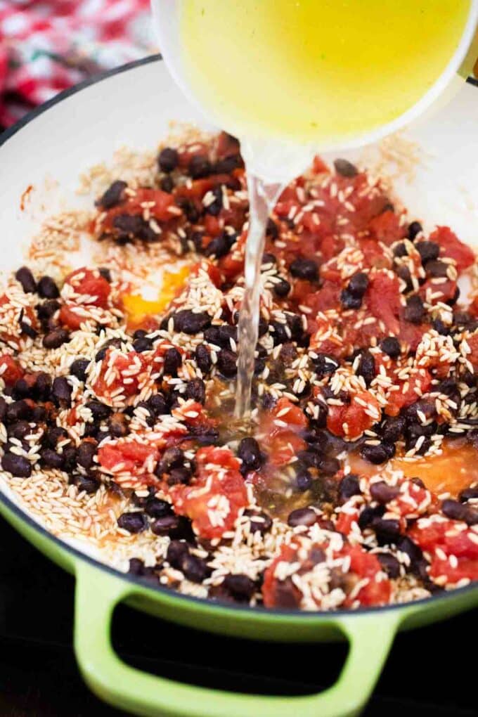 pouring broth into a skillet with rice beans and diced tomatoes