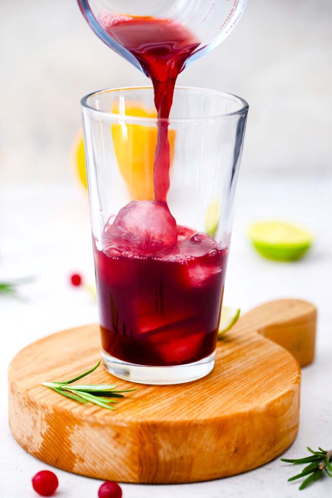 pouring cranberry juice over ice in a tall glass