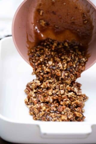pouring pecan pie mixture from a saucepan into a baking dish