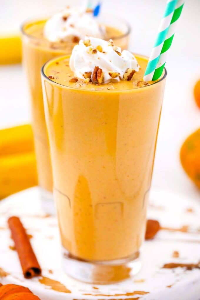two tall glasses with creamy pumpkin pie smoothie topped with whipped cream