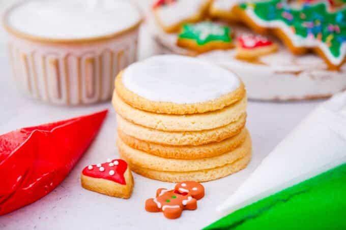 a stack of sugar cookies topped with royal icing with piping bags filled with royal icing next to them