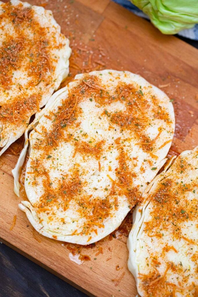 Seasoning cabbage steaks on a cutting board.