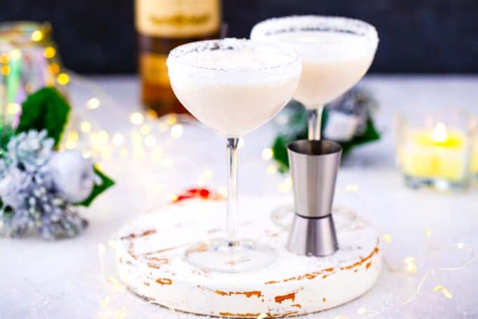 two glasses of white snowflake martini on a white stand with Christmas lights in the background