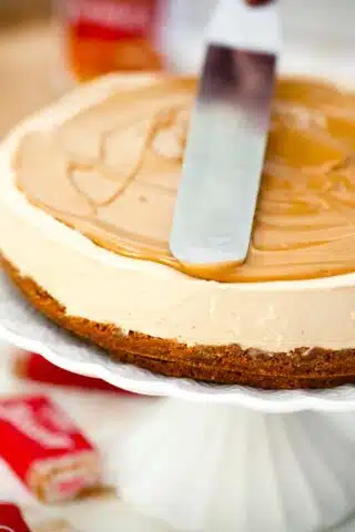 spreading cookie butter with a spatula on top of a biscoff cheesecake