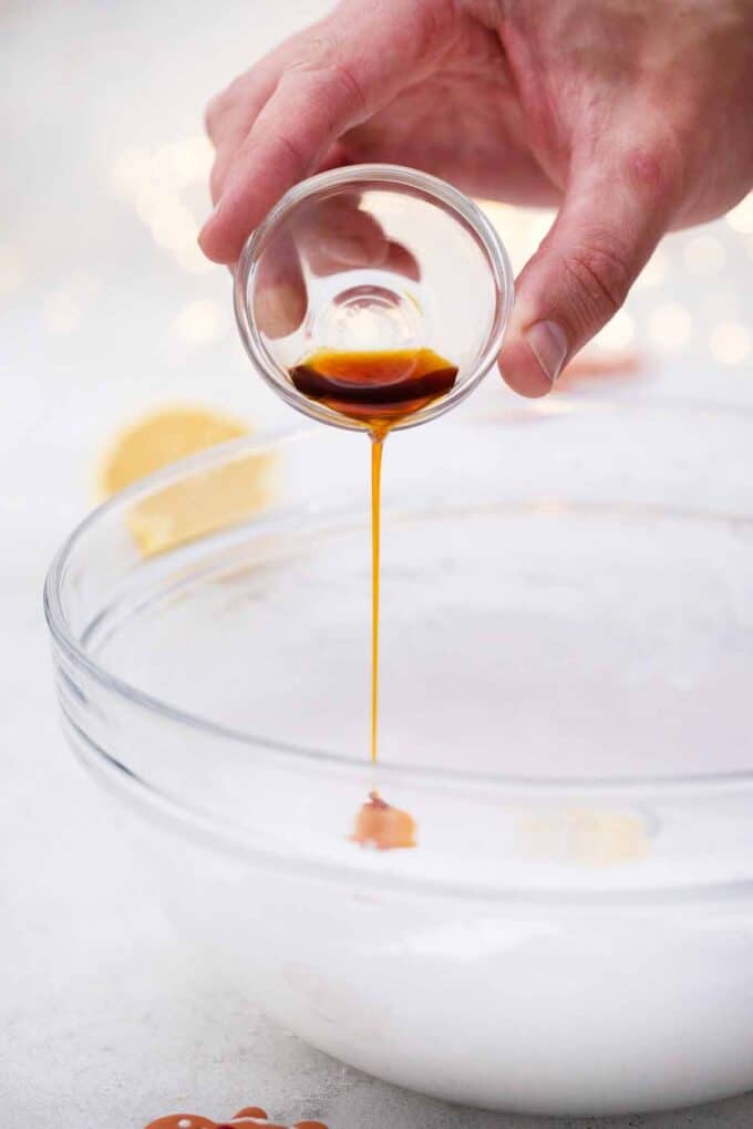 pouring vanilla extract into a bowl with fluffy egg whites