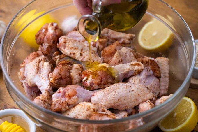 drizzling olive oil over raw wings in a bowl