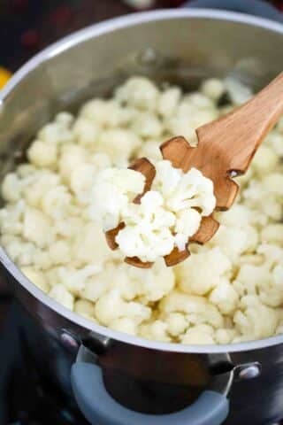boiling cauliflower florets and mixing them with a wooden spoon