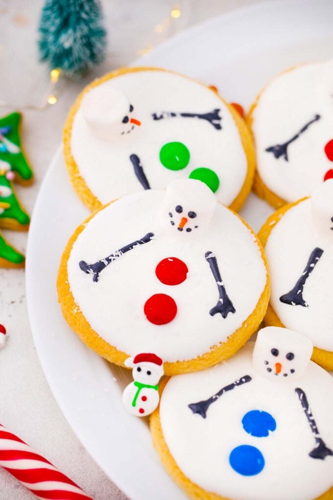 close shot of melted snowman cookies on a plate with candy cane next to it
