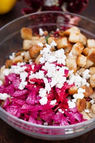 mixing croutons with feta cheese and pink radish in a bowl