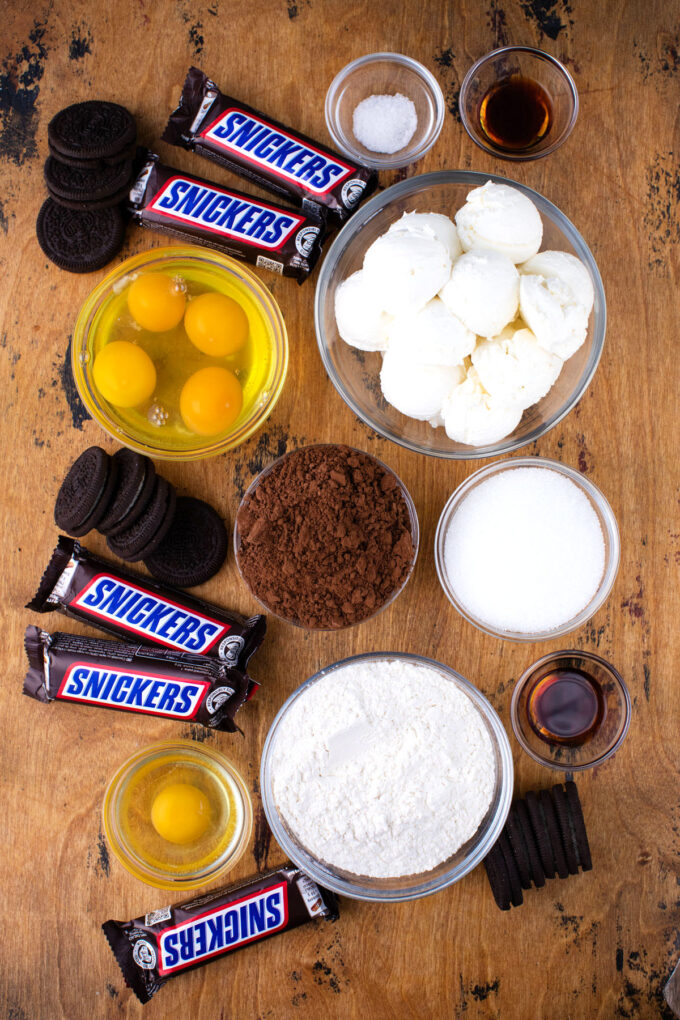 Overhead shot of slutty cheesecake brownie bars ingredients in bowls on a wooden surface.