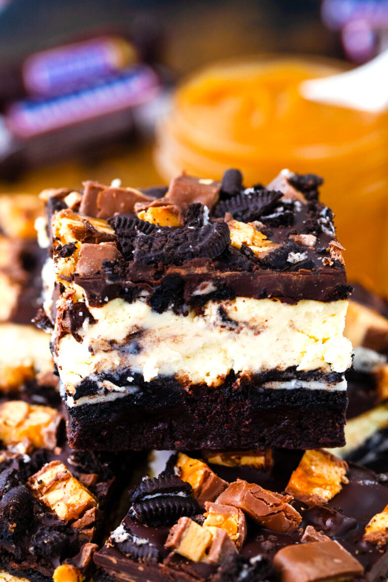 Slutty cheesecake brownie bars with brownie layer, cheesecake layer, Oreo layer, snickers, and melted chocolate.