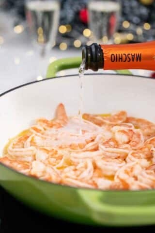 pouring champagne over shrimp in a pan