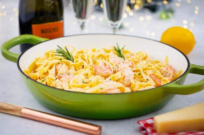 a skillet with of champagne shrimp scampi and champagne glasses next to it