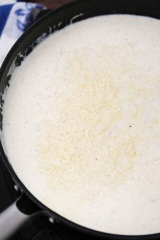 adding parmesan cheese to alfredo sauce in a skillet