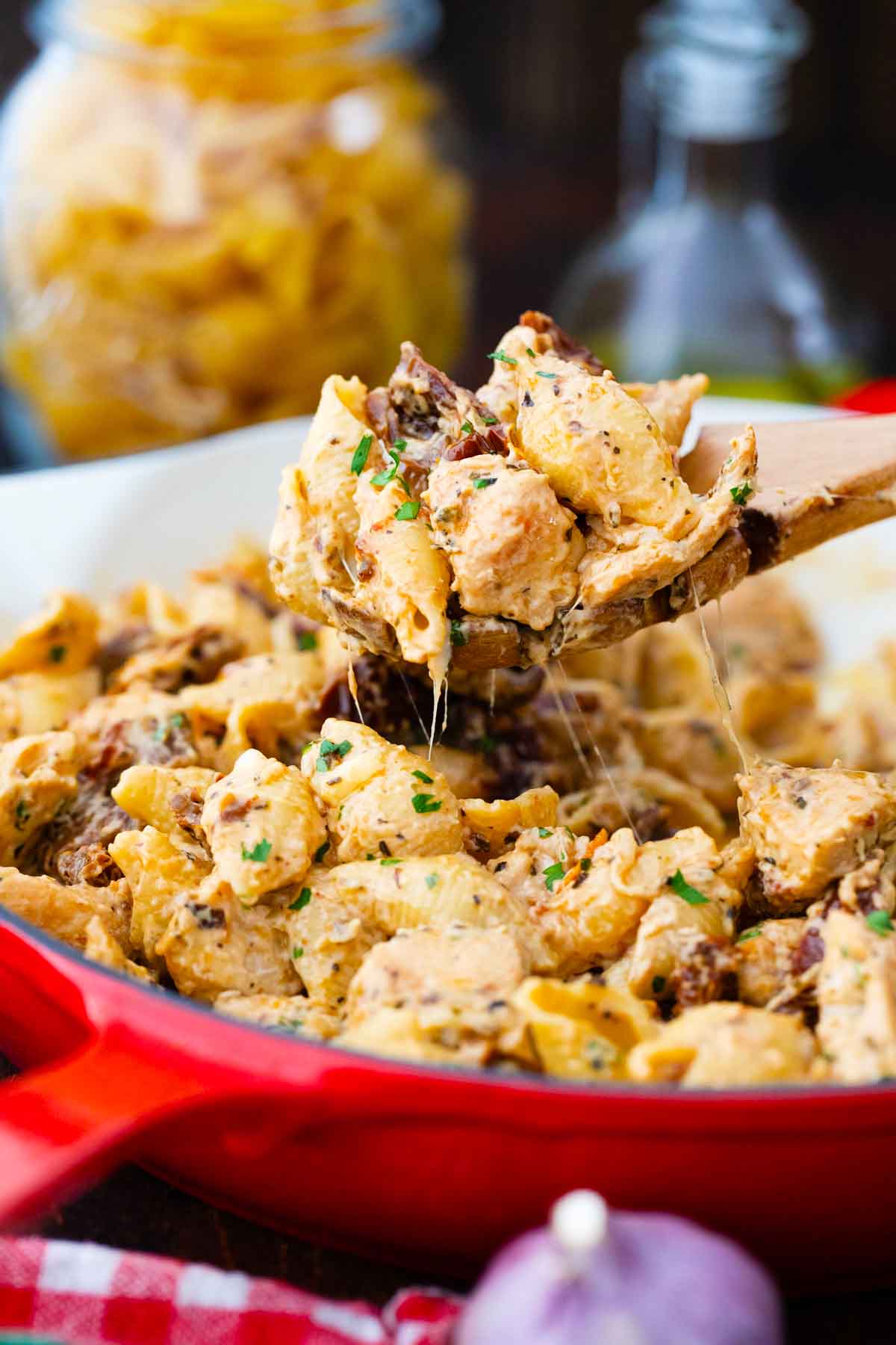 lifting a spoon of chicken mozzarella pasta from a red skillet