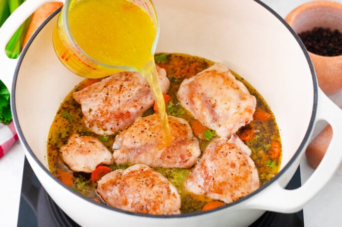Adding broth to a pot with veggies and chicken to make chicken noodle soup.