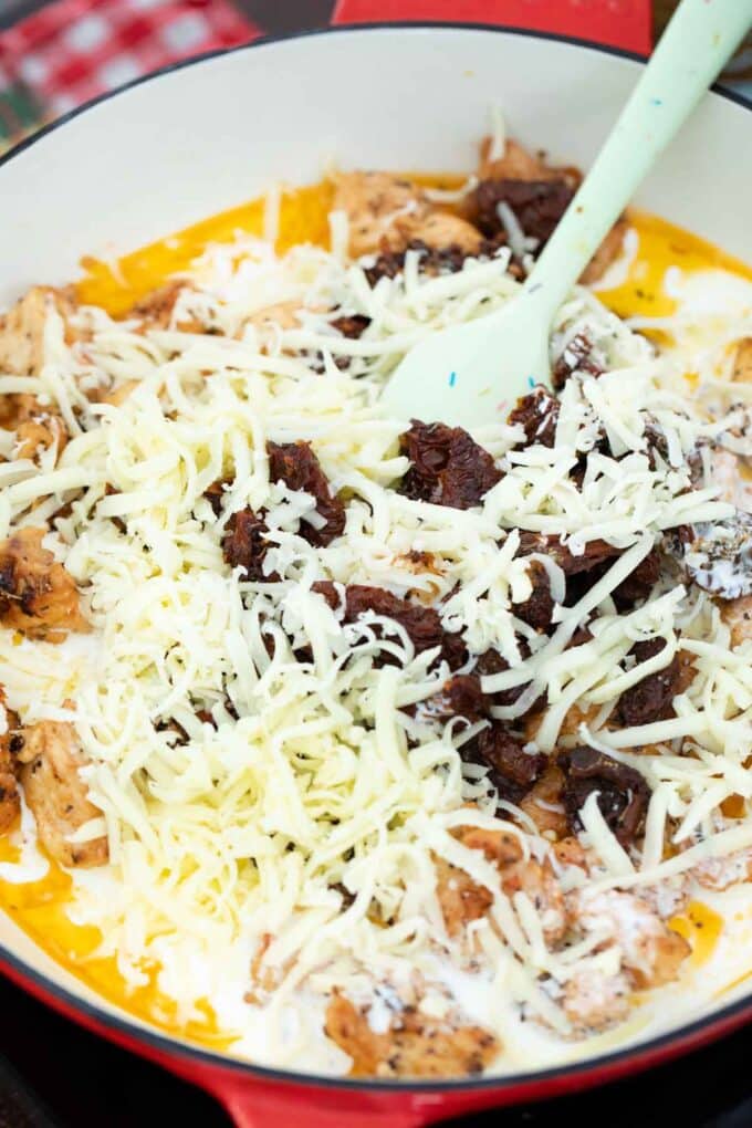adding shredded mozzarella cheese to a skillet with chicken and sun dried tomatoes