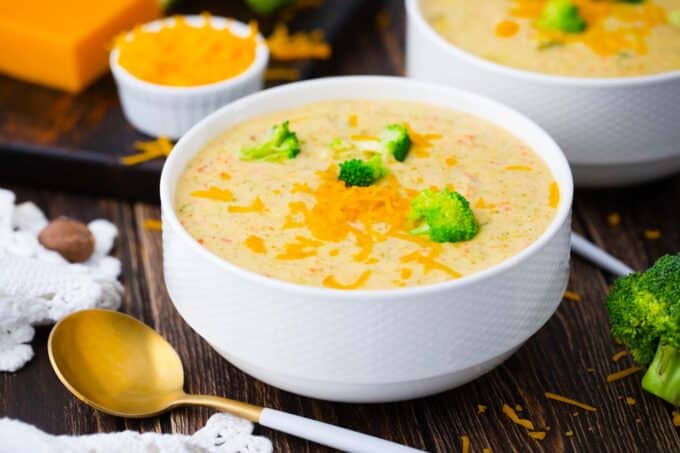 a bowl of panera bread broccoli cheddar soup topped with shredded cheddar cheese and mini broccoli