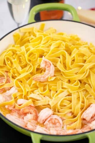 adding fettuccine pasta to a skillet with shrimp