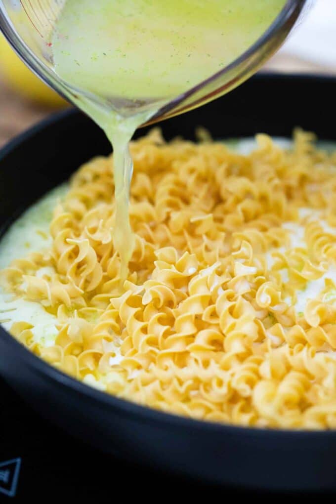 adding broth to pasta in a skillet