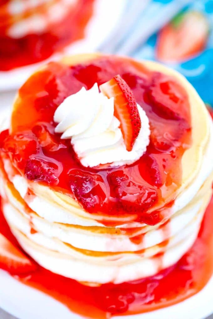 overhead shot of strawberry sauce and whipped cream on top of a stack of strawberry pancakes