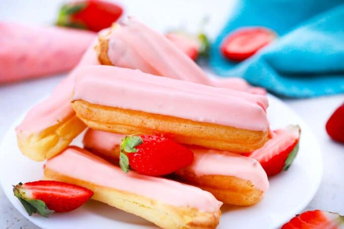 a stack of strawberry eclairs topped with pink chocolate and some fresh strawberries next to them