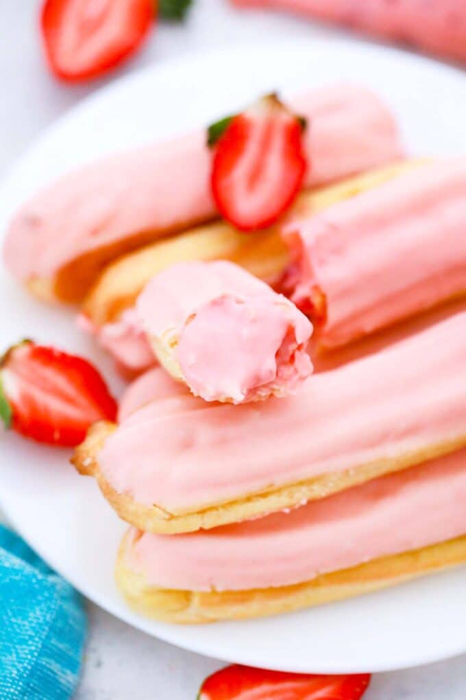 a stack of strawberry eclairs topped with pink chocolate and one sliced eclair revealing its creamy pink filling