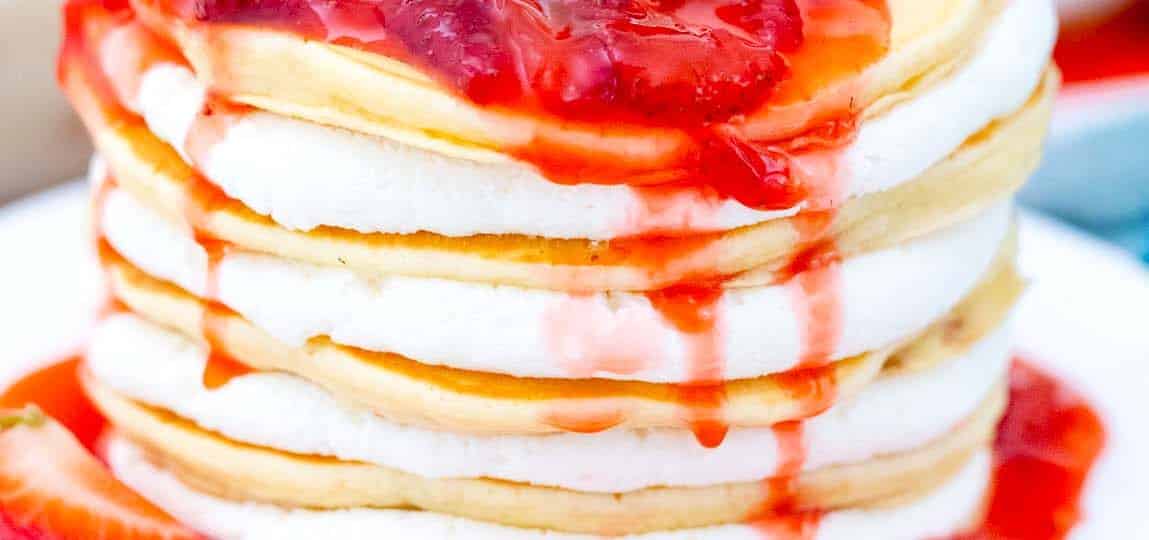 strawberry cheesecake pancakes with cheesecake filling and topped with strawberry sauce dripping over the, and whipped cream on top