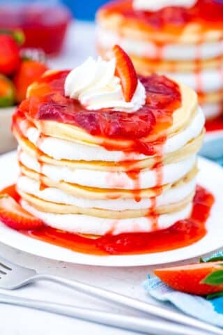 strawberry cheesecake pancakes with cheesecake filling and topped with strawberry sauce dripping over the, and whipped cream on top