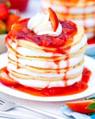 strawberry cheesecake pancakes with cheesecake filling and topped with strawberry sauce dripping over the, and whipped cream on top