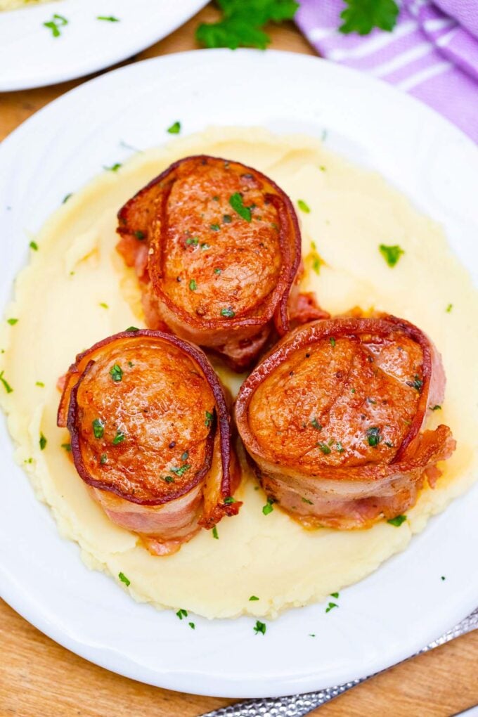 Overhead shot of juicy bacon pork medallions over mashed potatoes.
