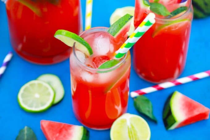 Glasses of boozy watermelon lemonade with green straws and lime wedges.