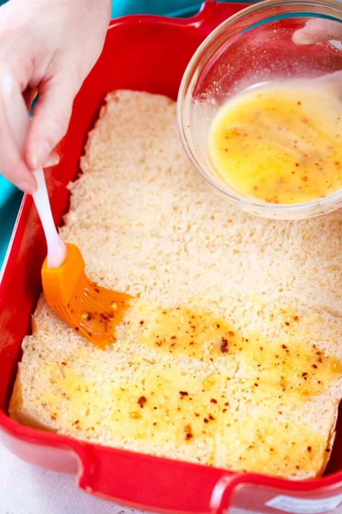 brushing with melted butter the bottom part of Hawaiian rolls in a pan