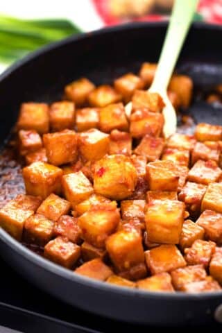 coating crispy tofu in a spicy sauce in a pan