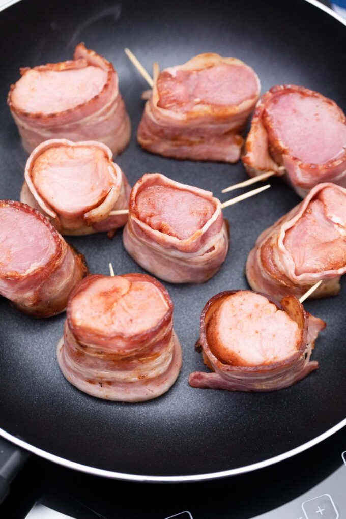 Bacon wrapped pork medallions in a pan.