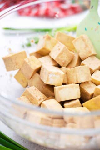mixing cuber firm tofu with marinade in a large bowl