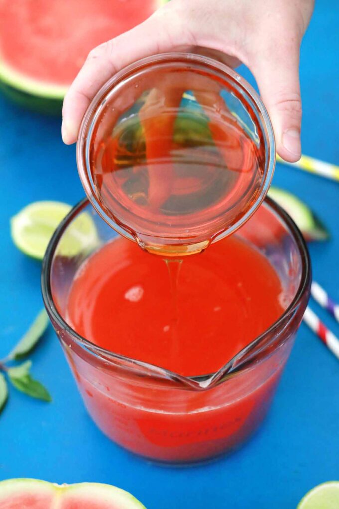 Adding syrup to boozy watermelon lemonade.