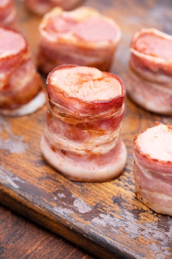 Bacon wrapped pork tenderloin pieces on a cutting board.
