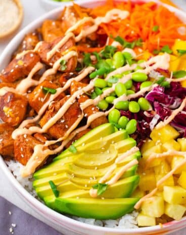 cooked salmon poke bowl with shredded red cabbage shredded carrot edamame pineapple mango and avocado with a spicy mayo drizzle and sesame seeds