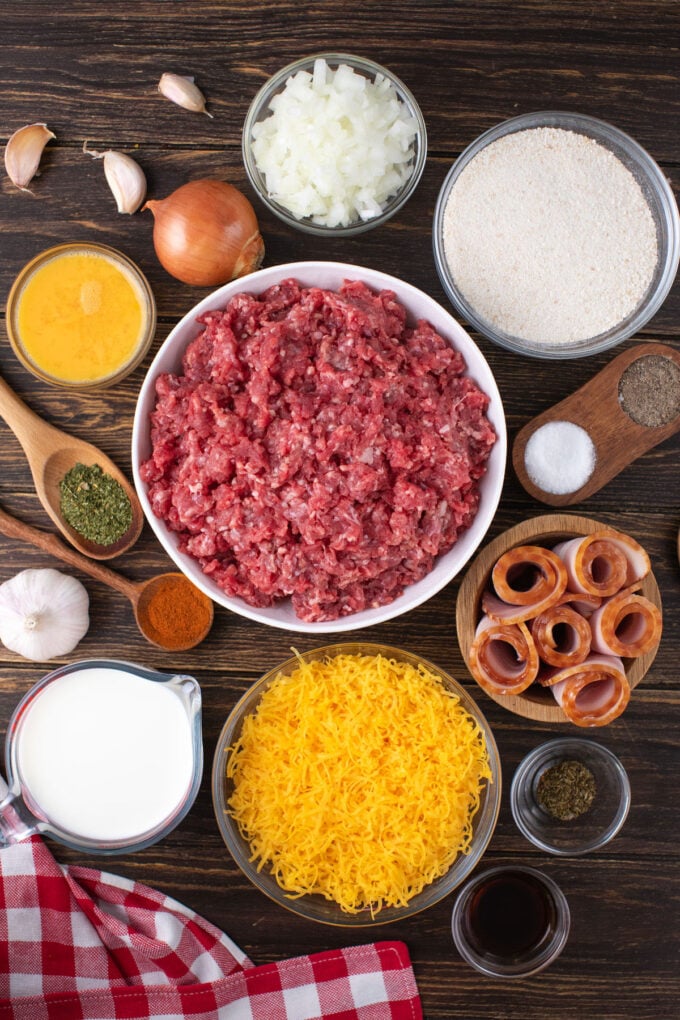Overhead shot of bacon wrapped meatloaf ingredients in bowls on a wooden table.