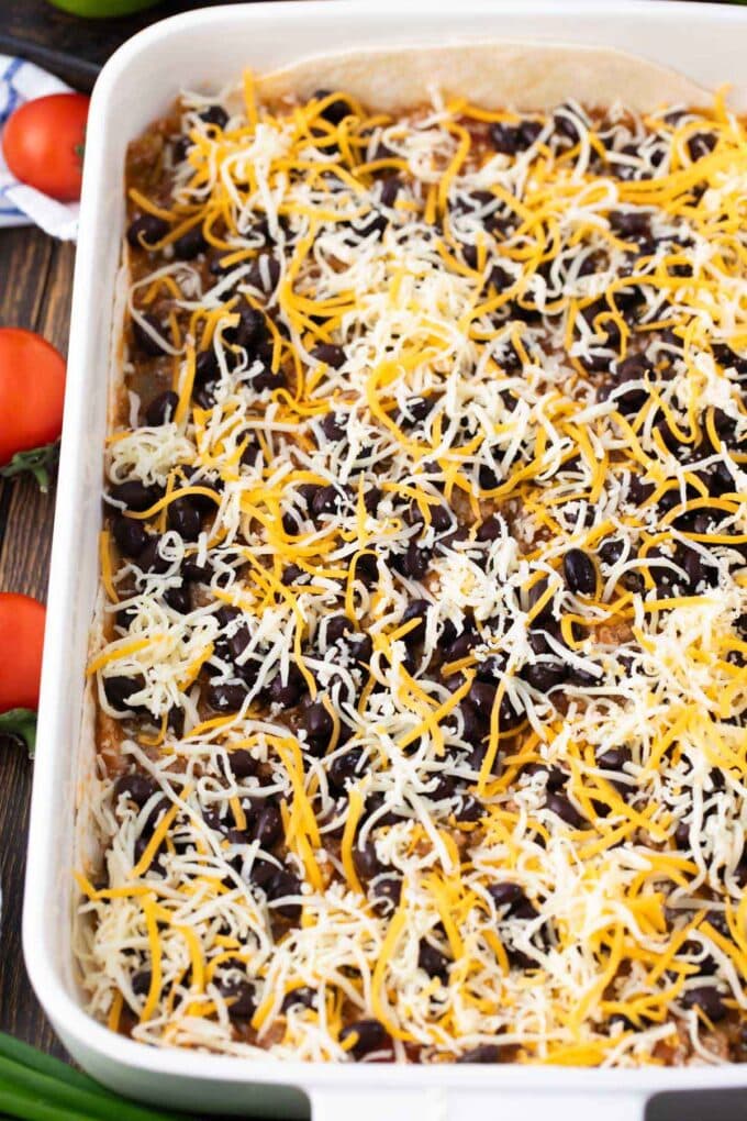 Assembling taco lasagna, adding black beans and shredded cheese.