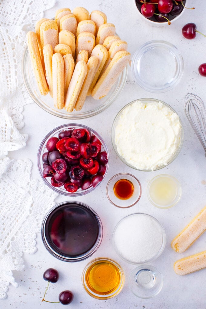 Overhead shot of cherry amaretto tiramisu ingredients in bowls on a white surface.