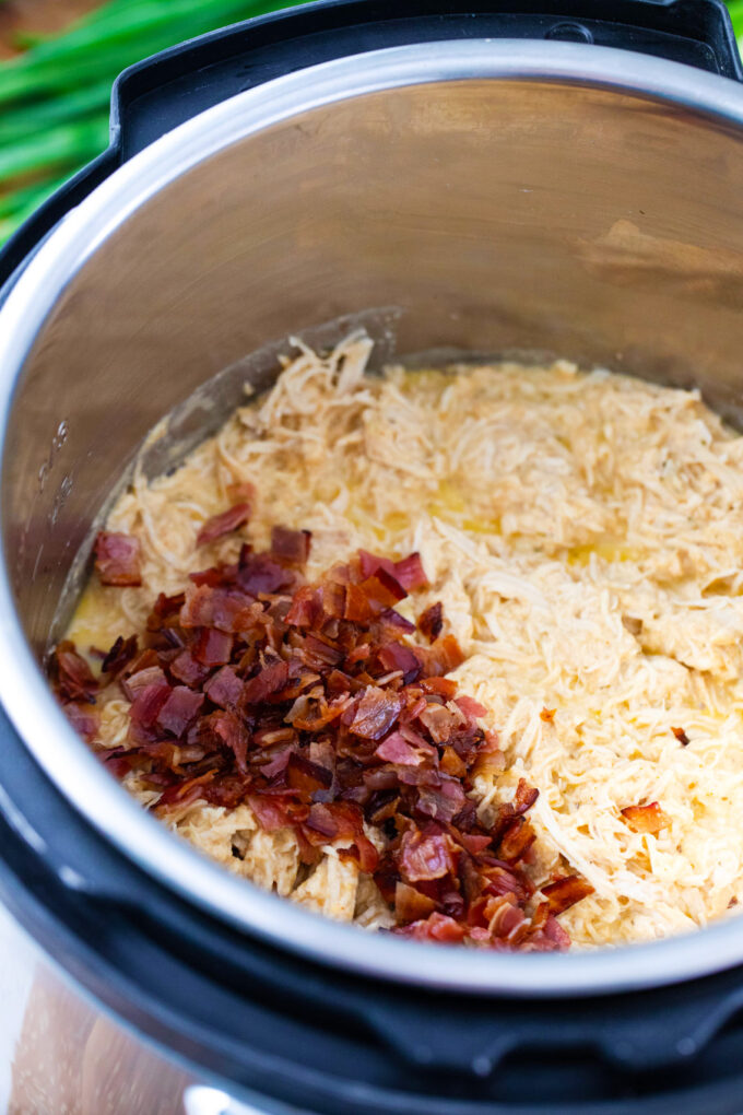 Adding bacon and cheese to Instant Pot crack chicken in the pot.