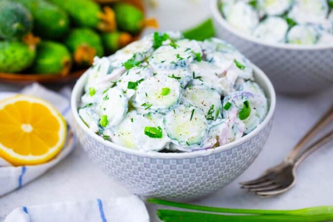 crunchy and creamy cucumber salad in two bowls with fresh cucumbers in the background